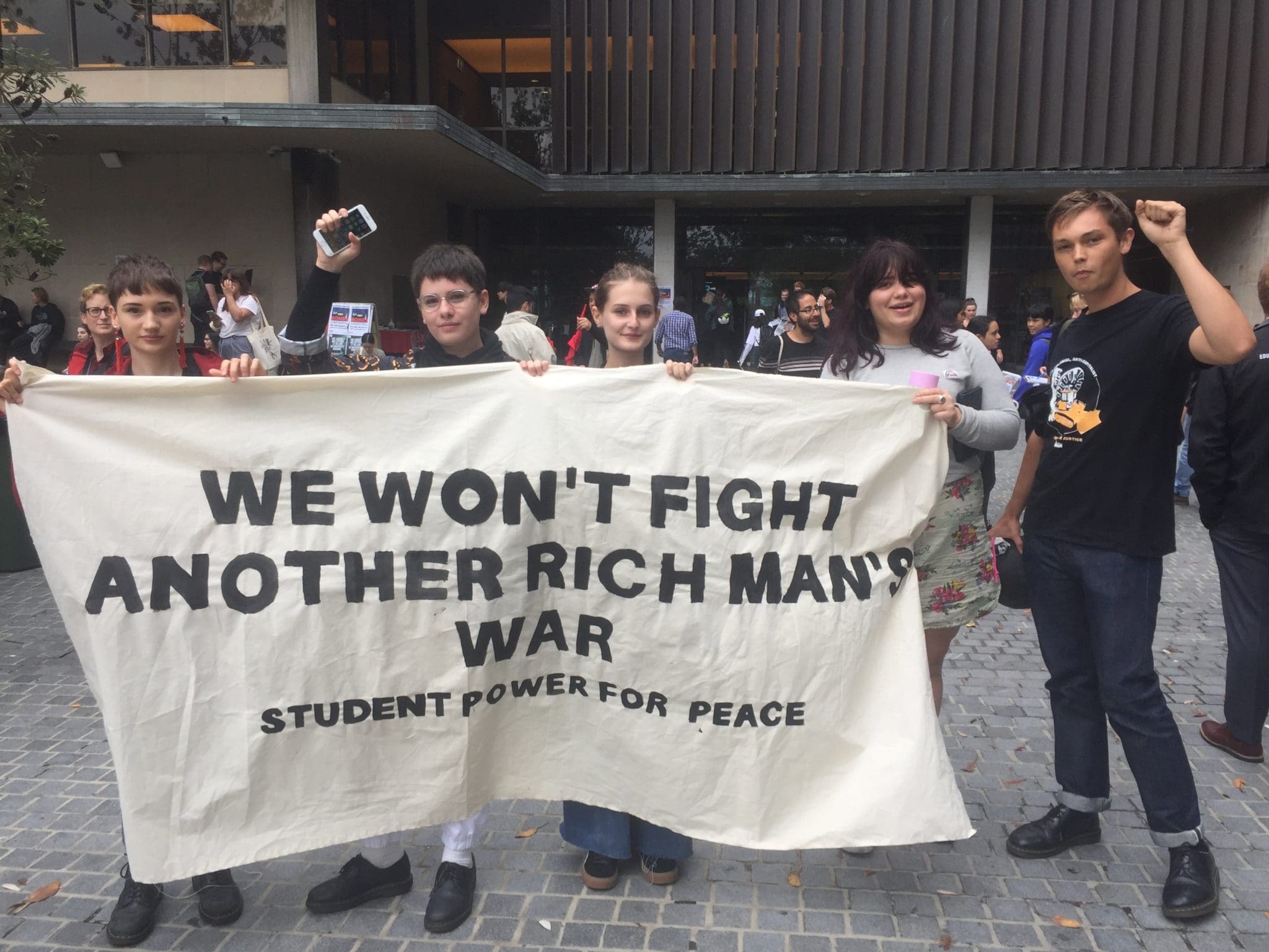 Image: student protestors hold up a banner saying "We won't fight another rich man's war." 