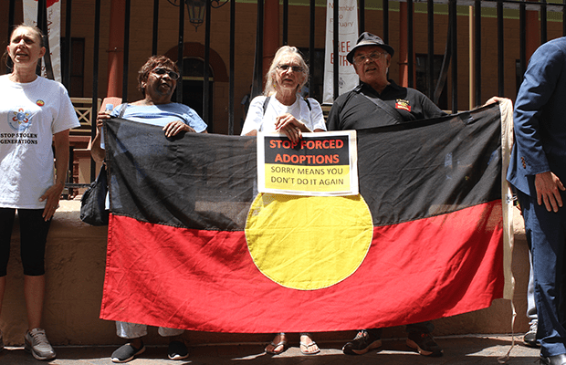 Hazel Collins, Aunty Doreen Webster, and Michael Welsh, speakers at the 2019 Sorry Day rally holding Aboriginal Flag outside NSW State Parliament