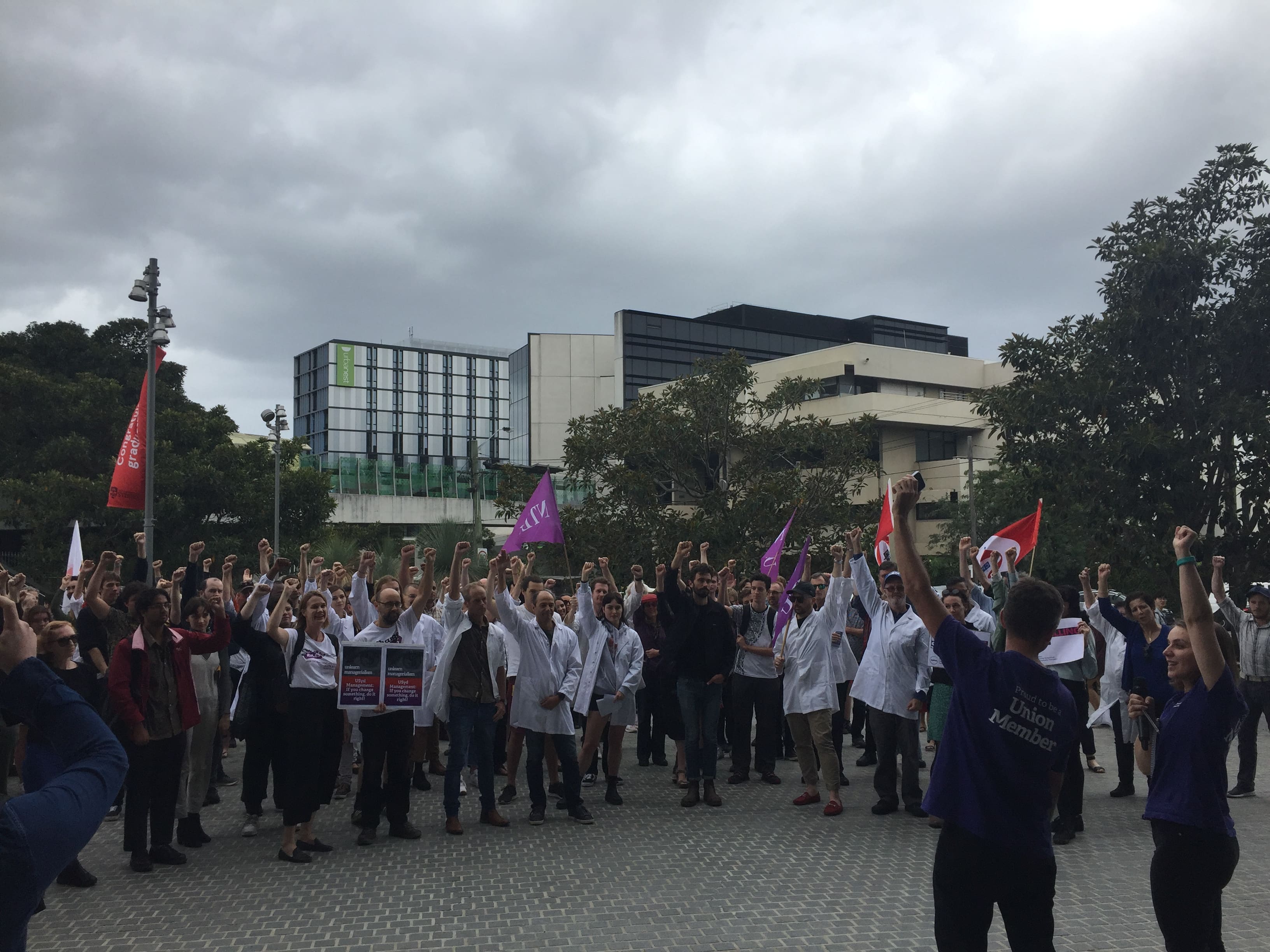 An NTEU motion of no confidence against Michael Spence and senior management passed unanimously. Staff and students pictured with fists raised.