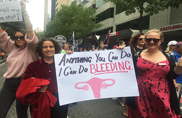 The march makes its way to Belmore Park in Sydney's CBD. Protesters hold a sign which reads "Anything you can do, I can do bleeding." 