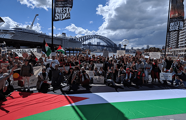 Image of protestors gathered with large Palestinian Flag in front of Sydney Harbour Bridge