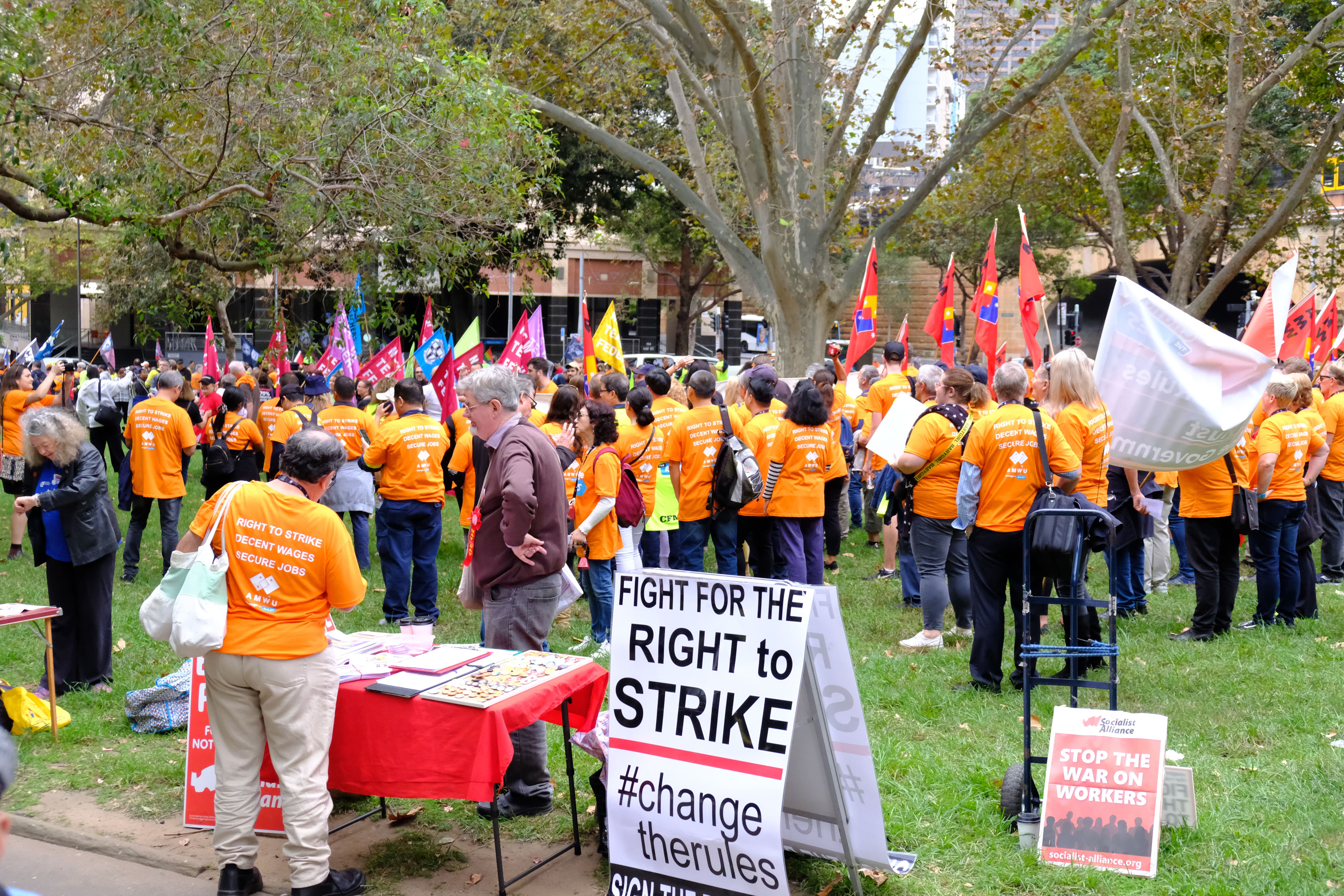 The March congregates in Belmore Park. The picture shows many AMWU workers holding flags in orange shirts.