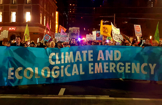 Protesters on George St hold up signs and a blue banner saying "climate and ecological emergency."