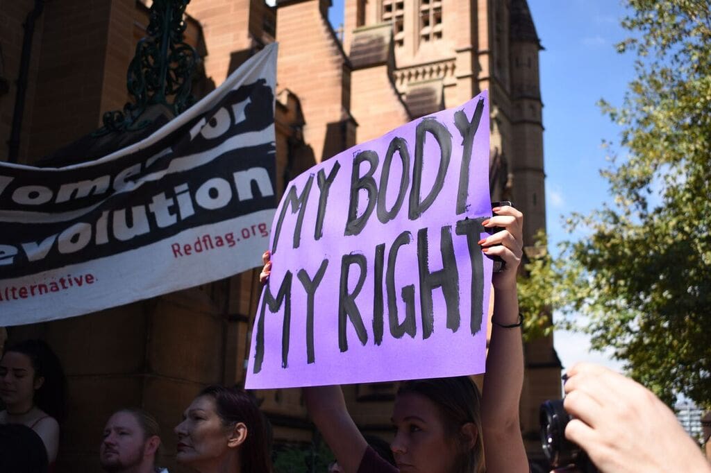 Protestor holding up a hand-painted, purple poster that reads: "My body my right", in front of St Mary's Cathedral