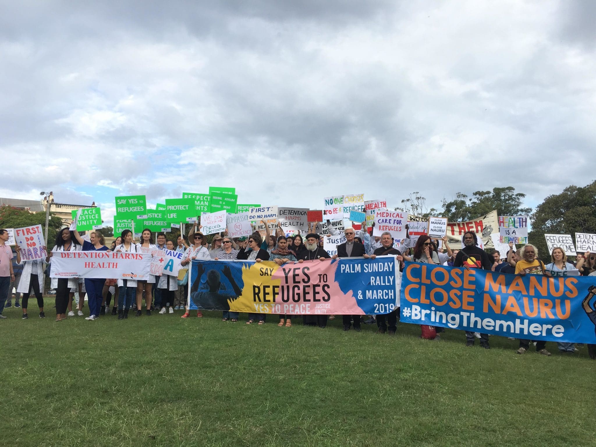 Crowd from the Palm Sunday Rally, holding banners that read "Say yes to refugees" and "Close Manus Close Nauru #Bringthemhere"