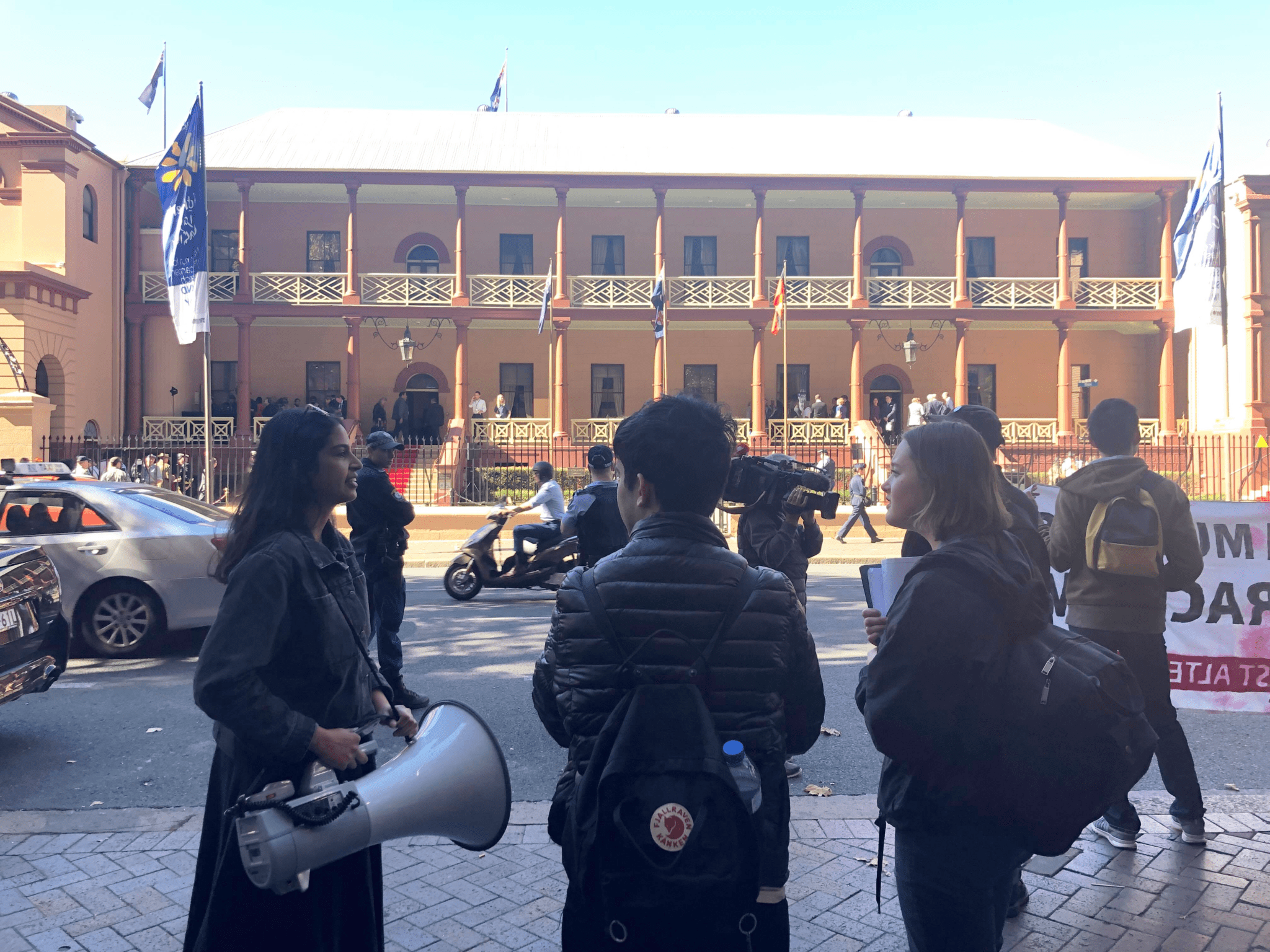 Activists Hersha Kadkol, Connor Parissis and Maddie Clark stand in front of the NSW State Parliament building.