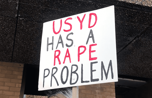 A photograph taken at the National Day of Action that reads "USYD HAS A RAPE PROBLEM"