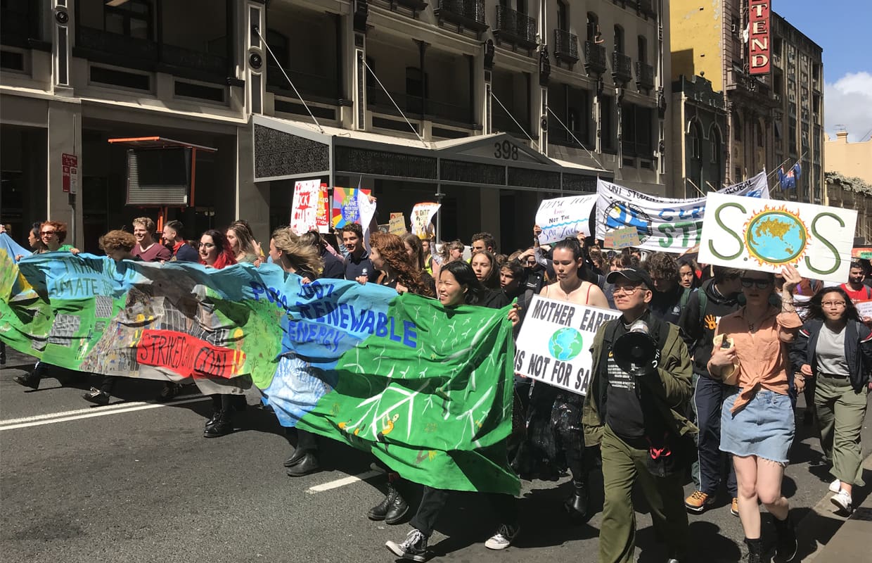 A group of people protesting and holding a large green and blue banner.
